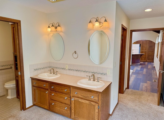 bathroom with double vanity, a sink, toilet, and tile walls