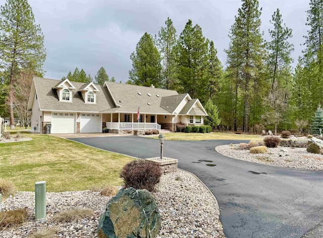 view of front of house featuring driveway, covered porch, an attached garage, and a front yard