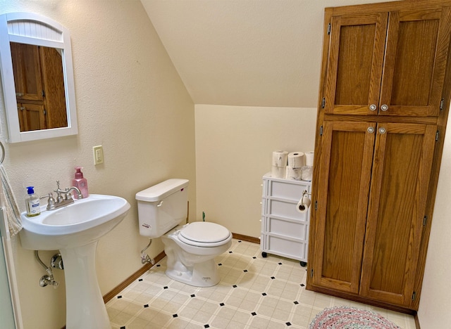 bathroom featuring baseboards, lofted ceiling, toilet, and a sink