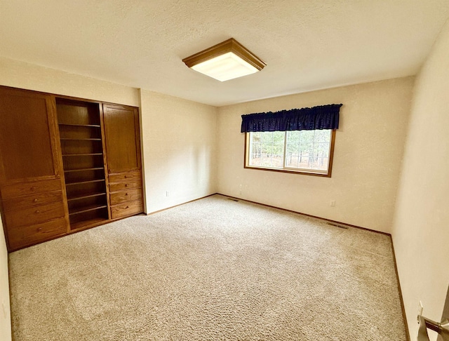 unfurnished bedroom featuring a closet, carpet flooring, a textured ceiling, baseboards, and visible vents