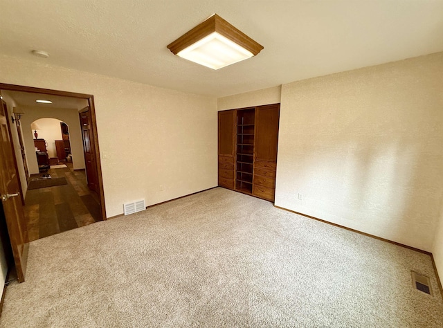 empty room with arched walkways, carpet floors, and visible vents
