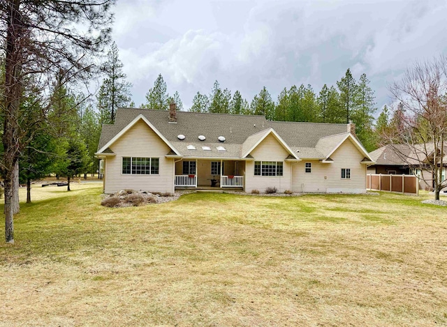 back of house featuring covered porch, roof with shingles, and a yard