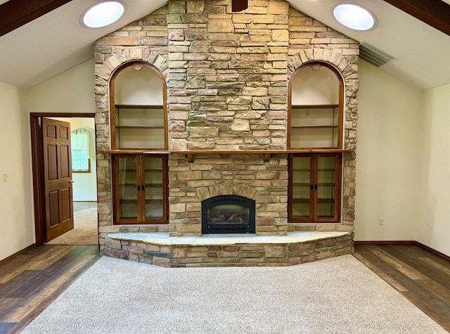 unfurnished living room featuring visible vents, baseboards, wood finished floors, a stone fireplace, and vaulted ceiling with beams