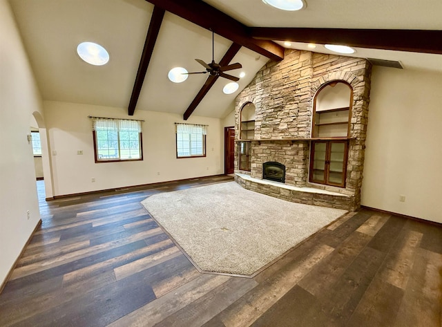 unfurnished living room featuring ceiling fan, wood finished floors, beamed ceiling, and a stone fireplace