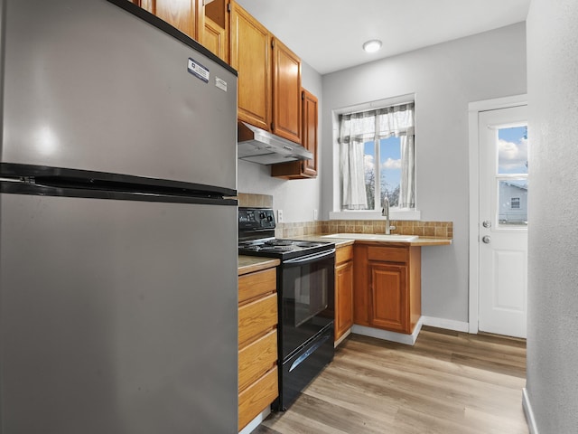 kitchen featuring a sink, freestanding refrigerator, under cabinet range hood, black electric range, and light wood-style floors