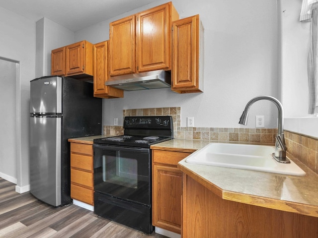 kitchen with light countertops, black range with electric cooktop, under cabinet range hood, a sink, and freestanding refrigerator