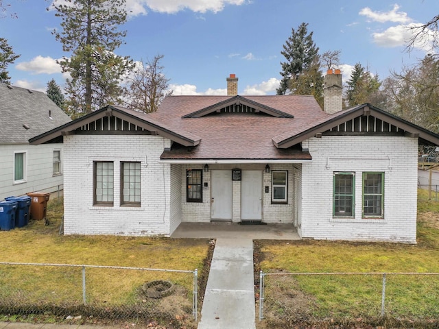 view of front of home featuring a front yard, covered porch, a chimney, brick siding, and a fenced front yard