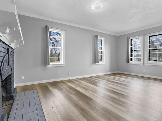 unfurnished living room featuring wood finished floors, a textured ceiling, a brick fireplace, baseboards, and ornamental molding