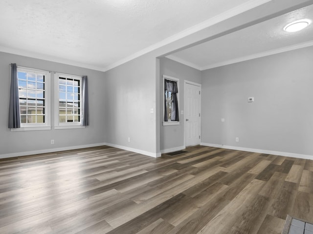 empty room featuring crown molding, baseboards, a textured ceiling, visible vents, and wood finished floors