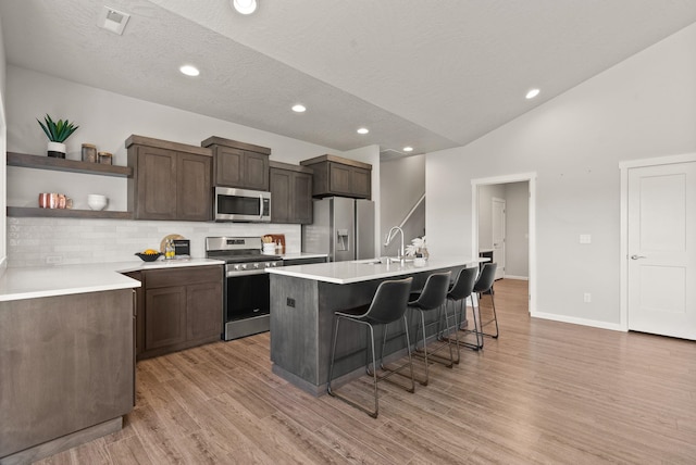 kitchen with an island with sink, open shelves, a kitchen bar, lofted ceiling, and appliances with stainless steel finishes
