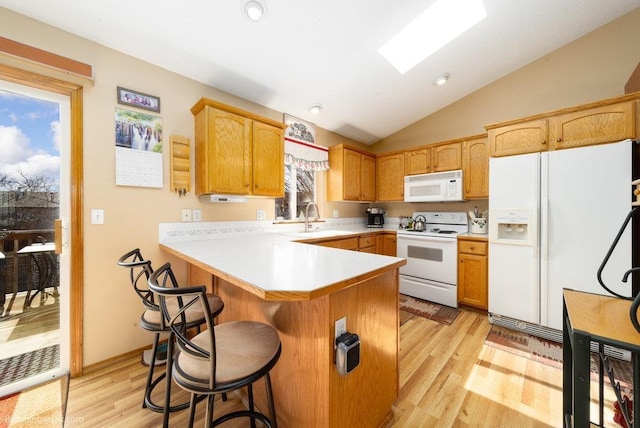 kitchen with a peninsula, white appliances, a kitchen breakfast bar, lofted ceiling with skylight, and light wood-style floors