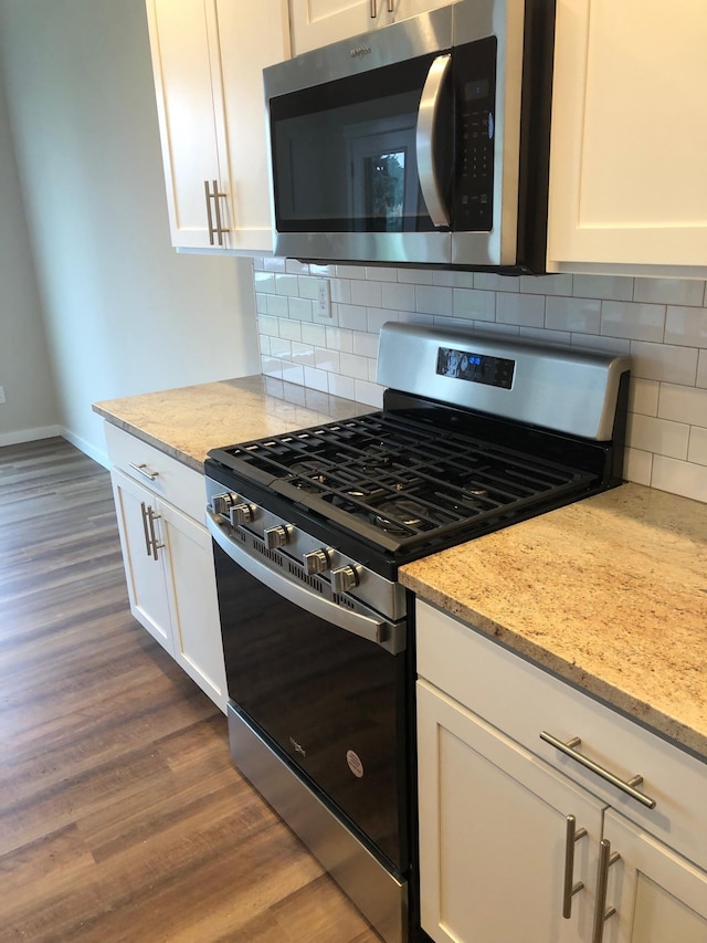 kitchen featuring white cabinetry, appliances with stainless steel finishes, light stone counters, and dark wood-type flooring