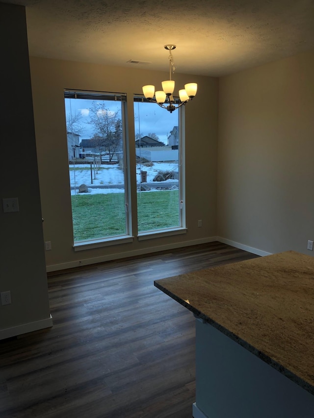 unfurnished dining area with baseboards, a notable chandelier, dark wood-type flooring, and a textured ceiling