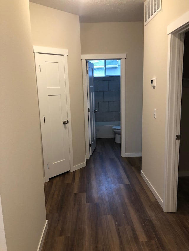 corridor featuring baseboards, visible vents, and dark wood-style flooring