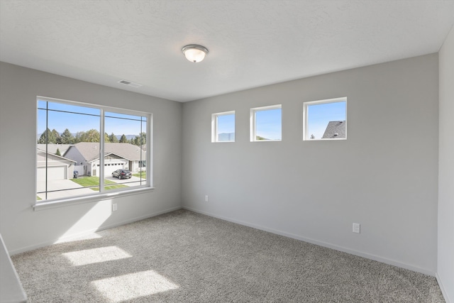 carpeted empty room featuring baseboards, a textured ceiling, and visible vents