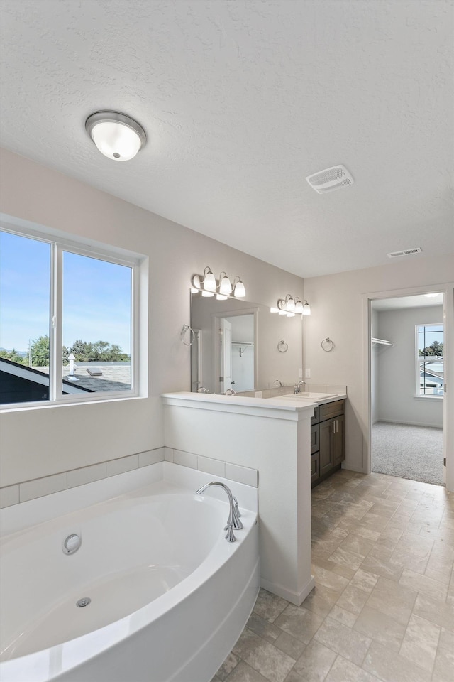 full bath with vanity, a textured ceiling, visible vents, and a bath