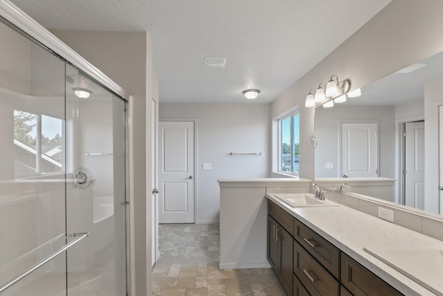 full bath with double vanity, a sink, stone finish flooring, and a shower stall