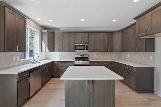 kitchen with a sink, light wood-type flooring, dark brown cabinetry, and appliances with stainless steel finishes
