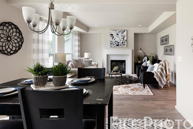 dining space with a notable chandelier, wood finished floors, and a glass covered fireplace