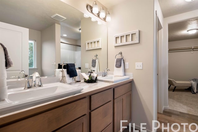bathroom featuring double vanity, visible vents, wood finished floors, and a sink