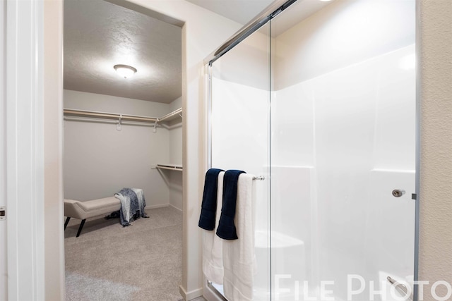 bathroom with a textured ceiling, a stall shower, and a walk in closet