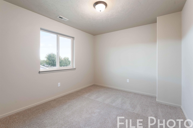 empty room featuring a textured ceiling, baseboards, light colored carpet, and visible vents