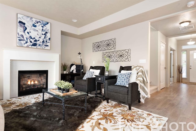 living area featuring visible vents, wood finished floors, and a glass covered fireplace