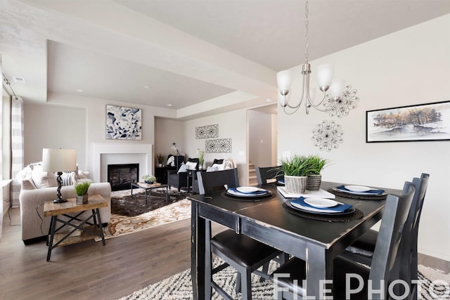 dining space featuring a fireplace, wood finished floors, a notable chandelier, and a raised ceiling