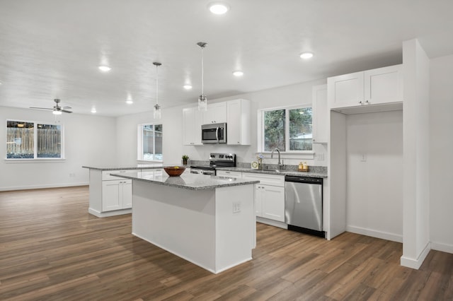 kitchen with a peninsula, appliances with stainless steel finishes, white cabinetry, a sink, and dark wood-style floors