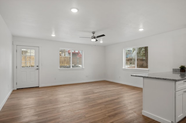 unfurnished living room with baseboards, ceiling fan, light wood finished floors, and a wealth of natural light