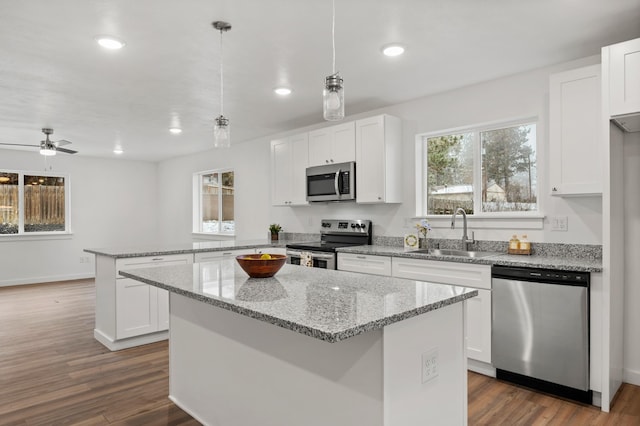 kitchen featuring dark wood-style flooring, stainless steel appliances, a kitchen island, a sink, and a peninsula