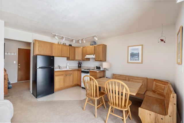 kitchen featuring light countertops, a sink, freestanding refrigerator, under cabinet range hood, and white stove