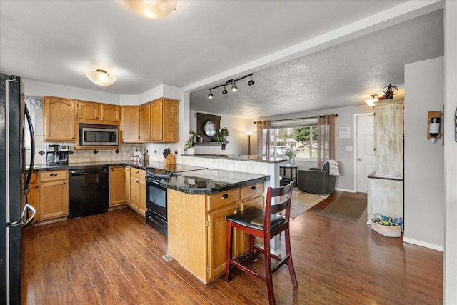 kitchen with tile counters, a peninsula, black appliances, and dark wood finished floors