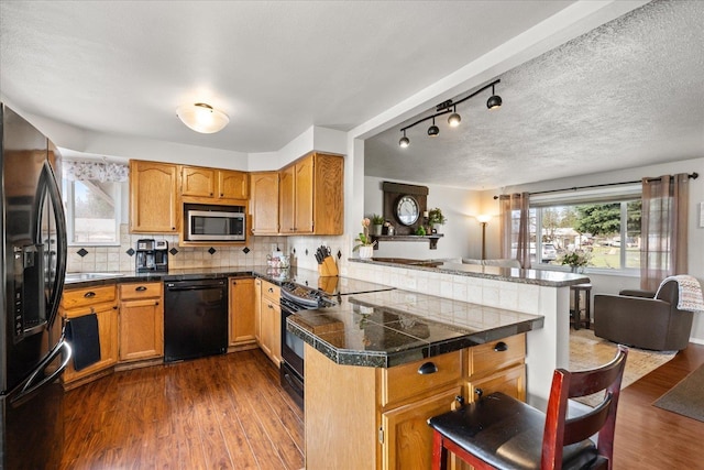 kitchen featuring dark wood finished floors, a peninsula, black appliances, and tile counters