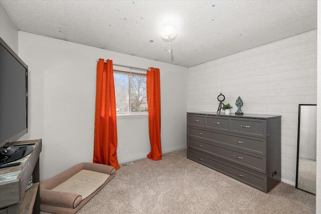 bedroom featuring visible vents, wood walls, light carpet, and a textured ceiling