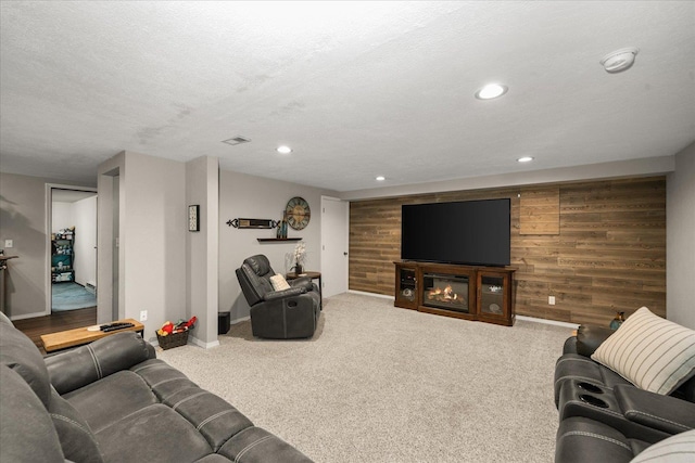 living area featuring a glass covered fireplace, recessed lighting, wooden walls, and visible vents