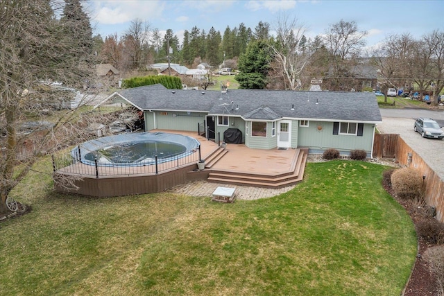 back of property with a shingled roof, a lawn, fence, a wooden deck, and a fenced in pool