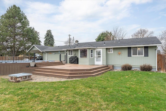 back of property with a deck, an outdoor fire pit, fence, and a lawn