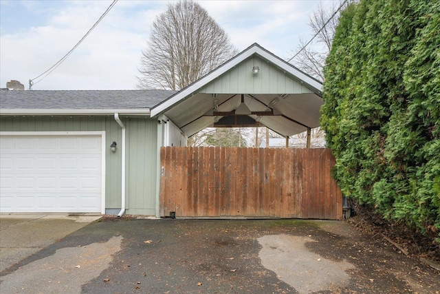 exterior space with an attached garage, fence, a shingled roof, and aphalt driveway