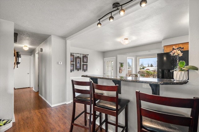 kitchen featuring a textured ceiling, a breakfast bar, black fridge, dark wood-style flooring, and baseboards