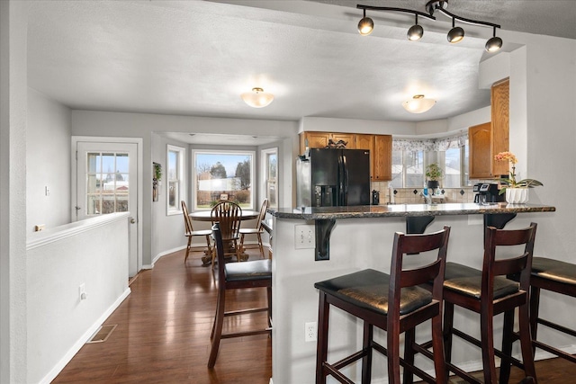 kitchen with brown cabinets, black fridge, dark wood-type flooring, and plenty of natural light