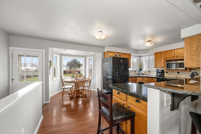 kitchen with tile countertops, a kitchen breakfast bar, black refrigerator with ice dispenser, stainless steel microwave, and decorative backsplash