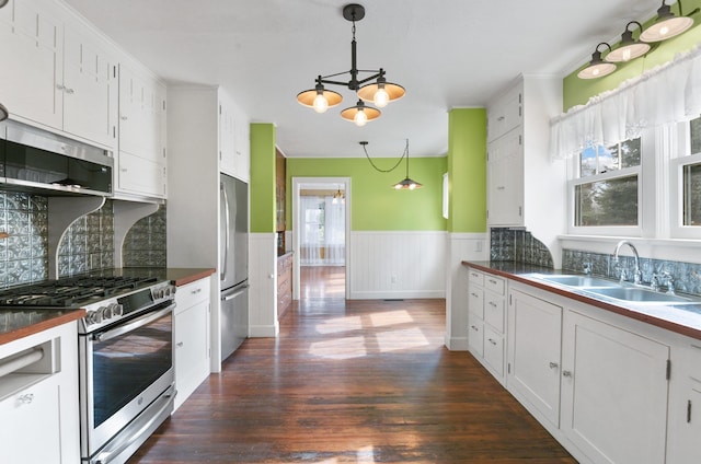 kitchen with an inviting chandelier, dark countertops, wainscoting, appliances with stainless steel finishes, and a sink
