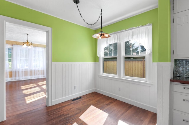 unfurnished dining area with dark wood-style floors, visible vents, an inviting chandelier, and a wainscoted wall