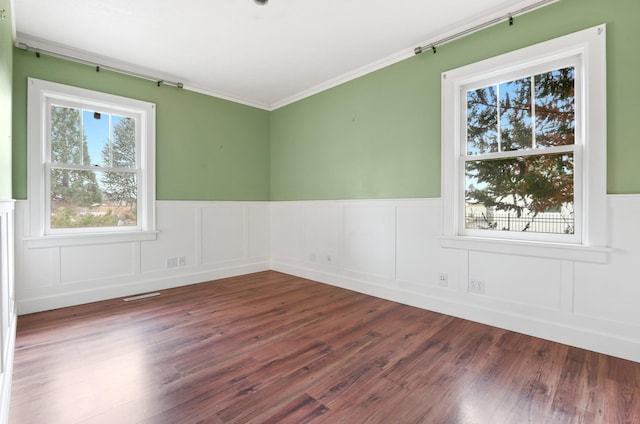 spare room with dark wood-type flooring, visible vents, ornamental molding, and a wainscoted wall