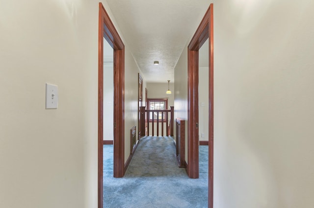 hallway featuring a textured ceiling, baseboards, and carpet