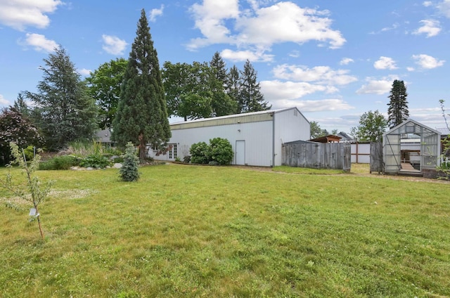 view of yard with a greenhouse, an outbuilding, and fence