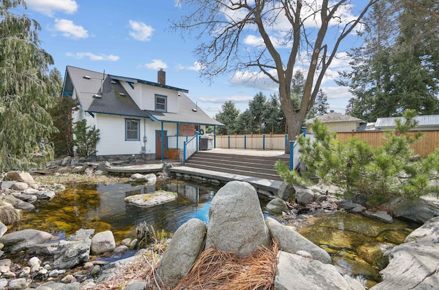 rear view of house featuring a chimney, a small pond, and fence
