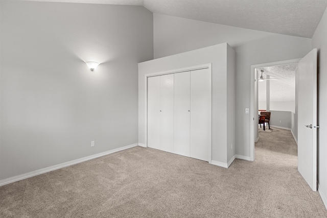 unfurnished bedroom featuring lofted ceiling, light carpet, a closet, a textured ceiling, and baseboards