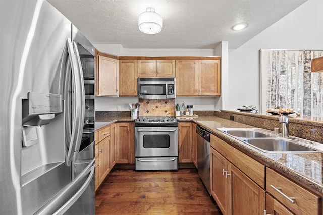 kitchen with appliances with stainless steel finishes, a sink, dark wood-style floors, a textured ceiling, and stone counters